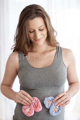 Buy stock photo Cropped shot of a young pregnant woman holding baby shoes while standing in her home