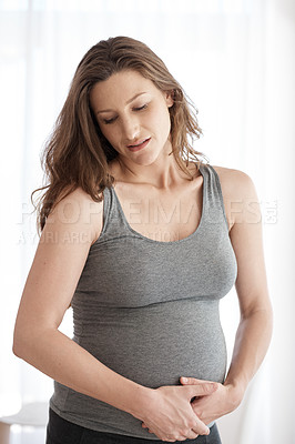Buy stock photo Cropped shot of a young pregnant woman holding her stomach in pain while standing in her home