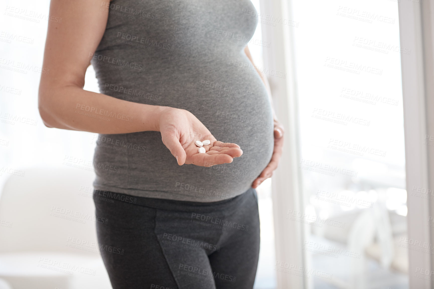 Buy stock photo Cropped shot of a pregnant woman holding tablets while standing in her home