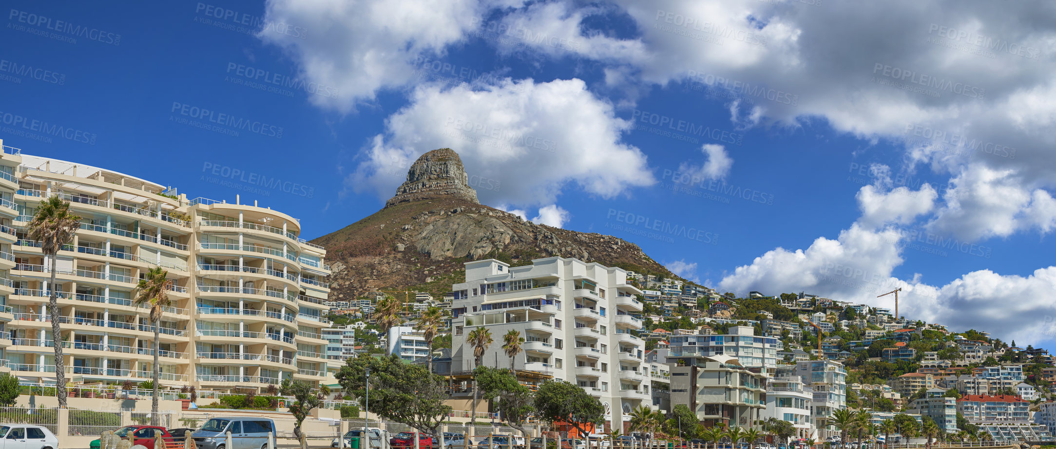 Buy stock photo Buildings, mountain and blue sky with clouds in city for travel, vacation and adventure. Urban landscape, summer and cars on street for holiday in coastal town for scenic view, greenery and tourism