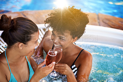 Buy stock photo Cropped shot of two young women enjoying a glass of champagne in a jacuzzi