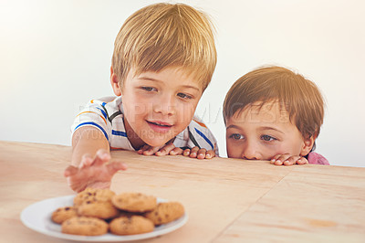 Buy stock photo Kids, boys and smile for cookies in home with stealing, peeking and childhood fun in at dining room table. Siblings, children and happy for biscuits, snack and baked goods in kitchen of apartment