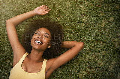 Buy stock photo Shot of a young woman laughing while relaxing on the grass