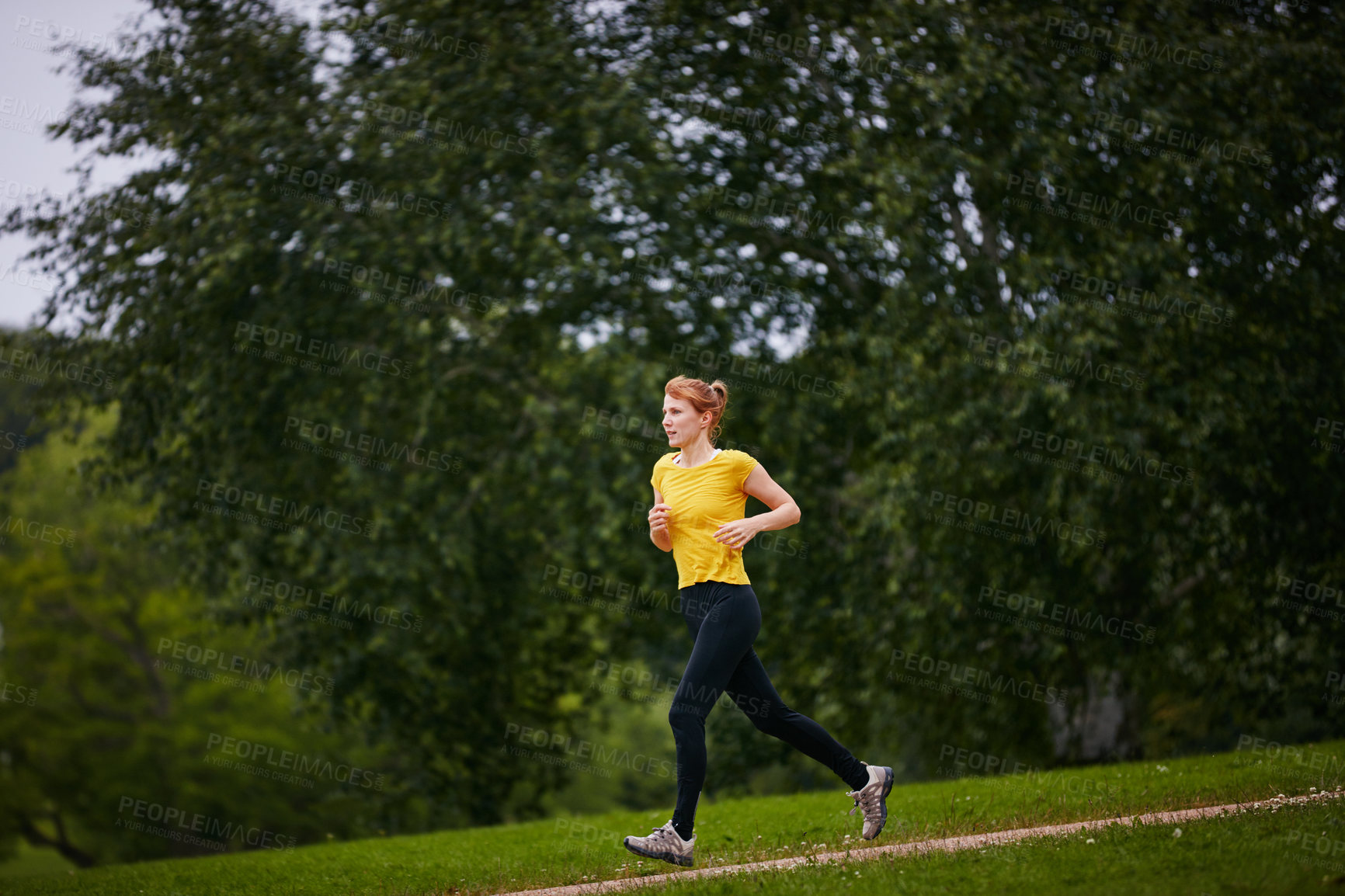 Buy stock photo Shot of a woman jogging along a foothpath in a park