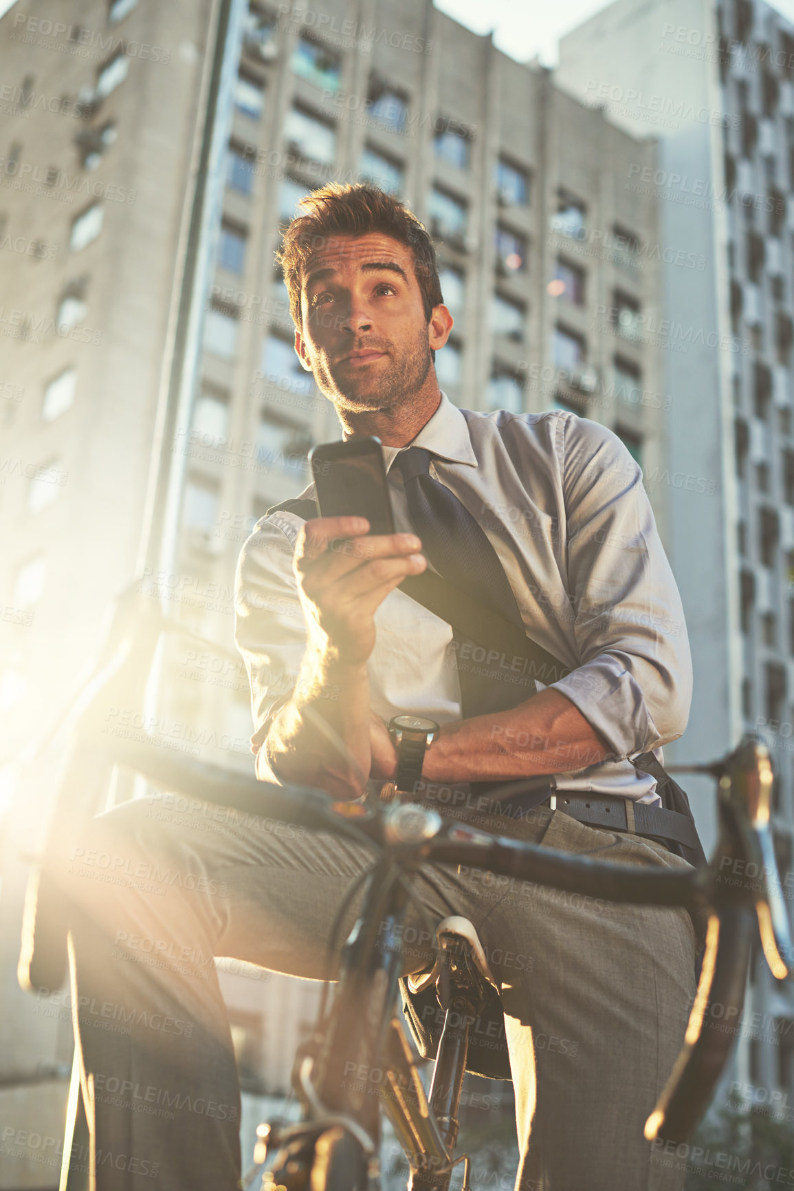 Buy stock photo Shot of a businessman using his cellphone while commuting to work with his bicycle