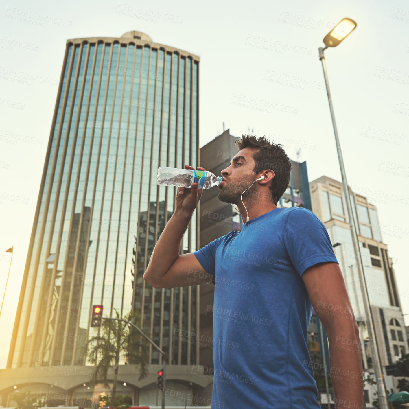 Buy stock photo A young man drinking from his water bottle while out running in the city