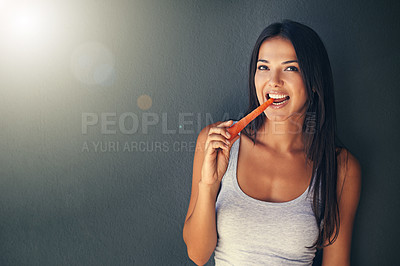 Buy stock photo Shot of a beautiful young woman biting into a carrot