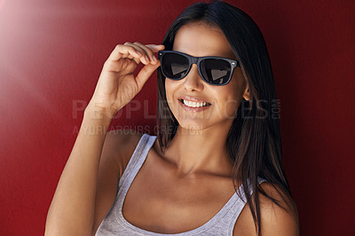 Buy stock photo Shot of an attractive young woman wearing sunglasses against a red background