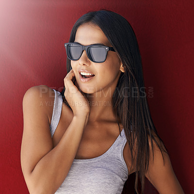 Buy stock photo Shot of an attractive young woman wearing sunglasses against a red background