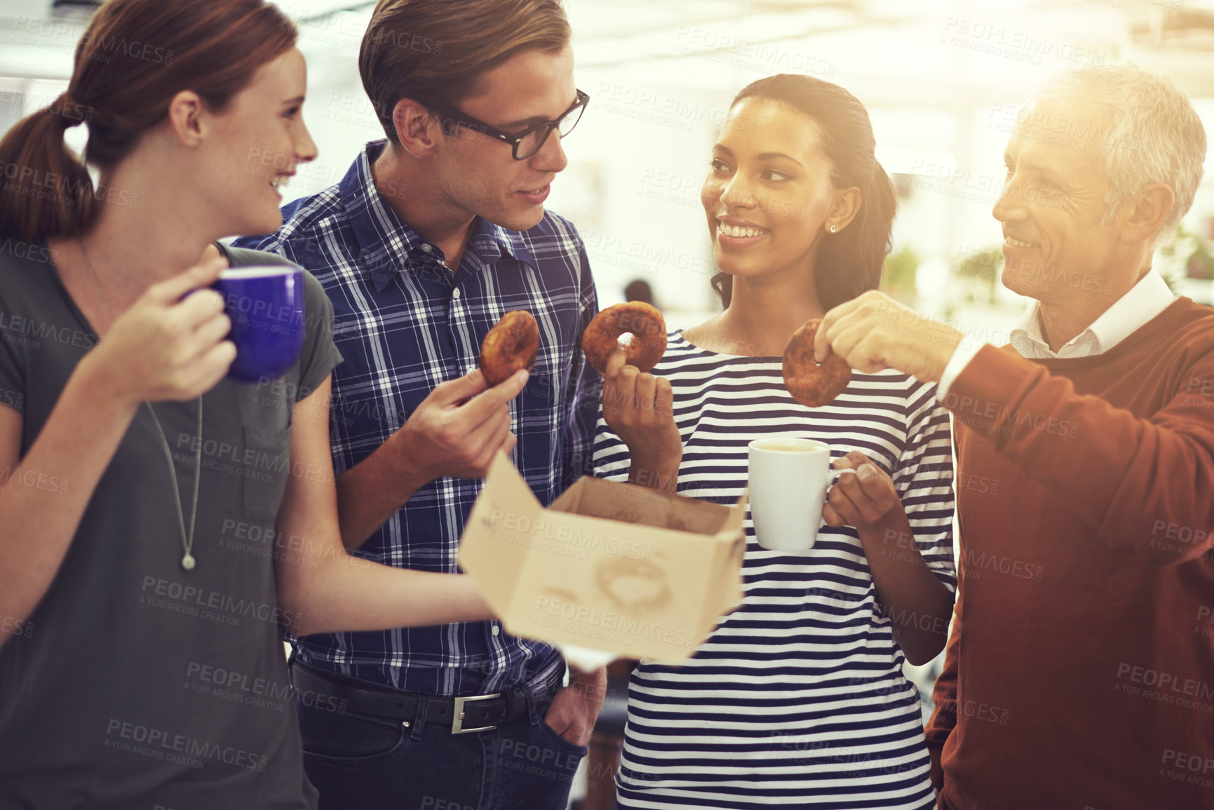 Buy stock photo Shot of a group of coworkers eating donuts while standing in an office
