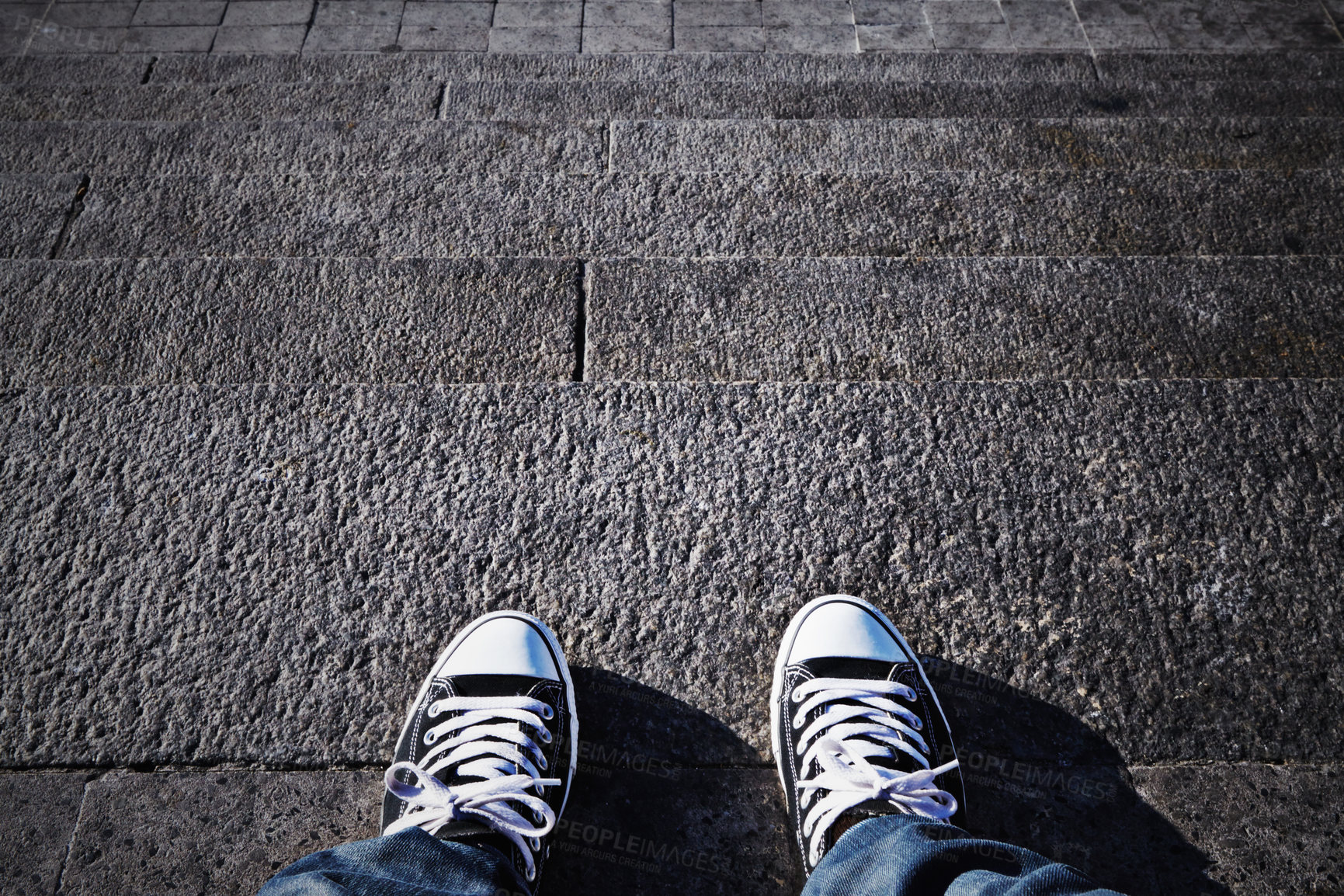 Buy stock photo Feet of a person wearing sneakers while standing or sitting on steps outside. Above of a pair of canvas shoes on a grey dark concrete paved staircase. A unisex individual in trendy streetwear fashion