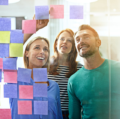 Buy stock photo Cropped shot of three business colleagues looking at sticky notes on a glass wall