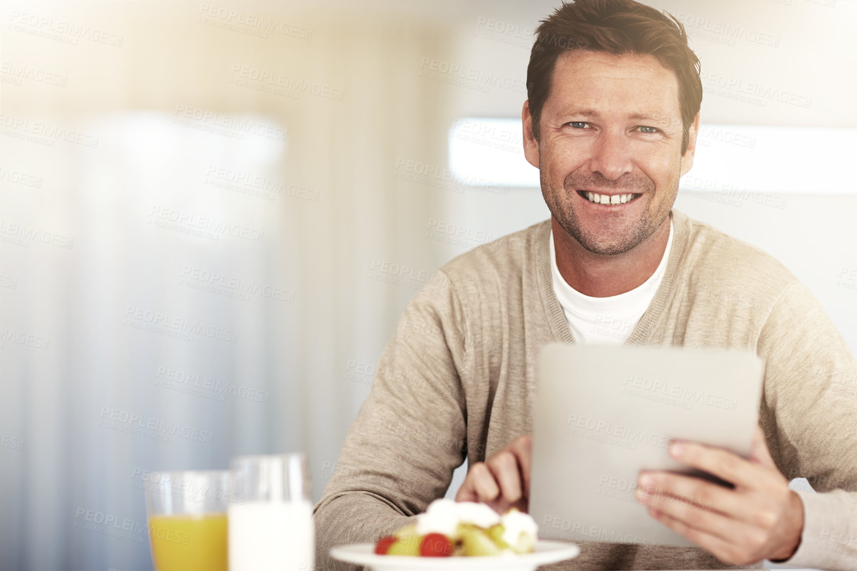 Buy stock photo Cropped portrait of a man using his tablet while eating breakfast at home