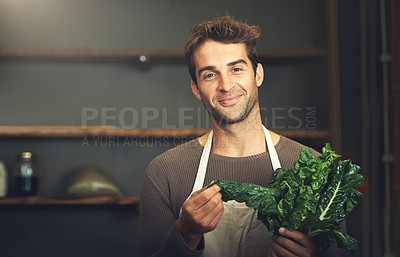 Buy stock photo Shot of a young man holding a bunch of spinach in his kitchen
