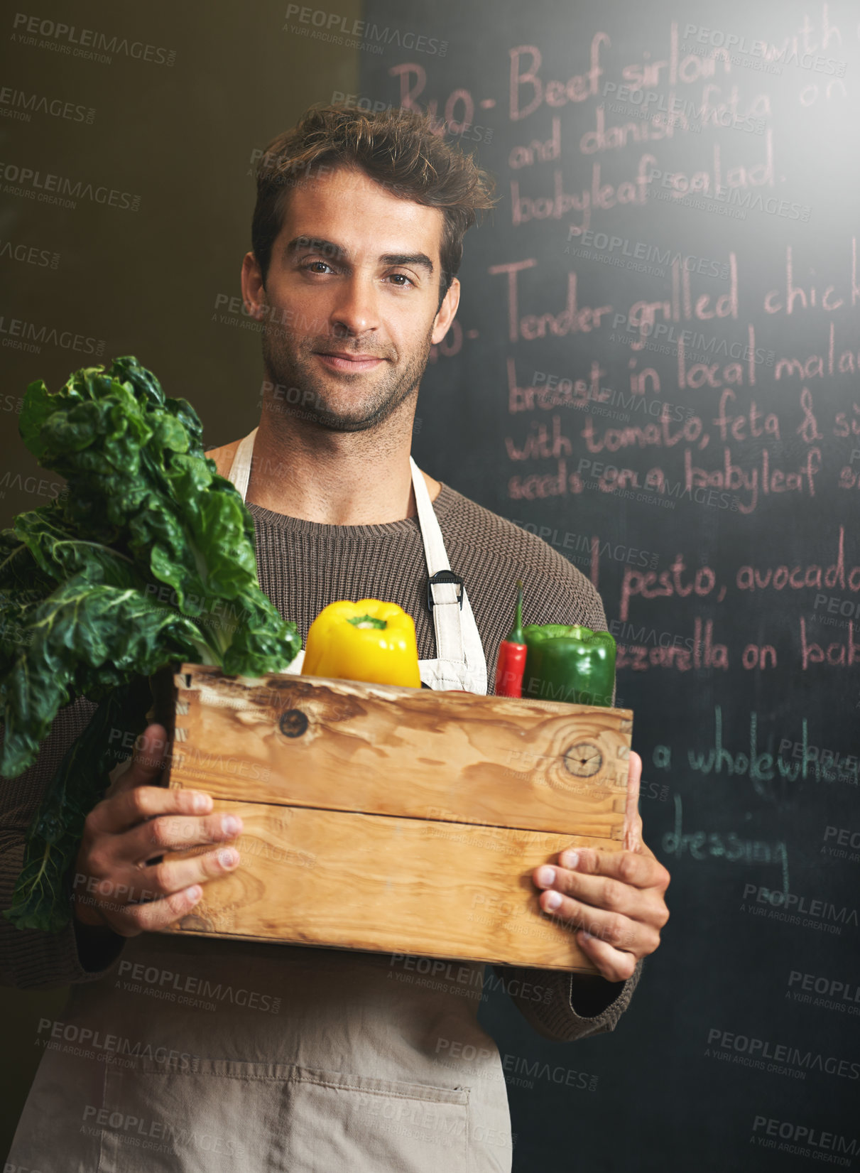 Buy stock photo Shot of a young man holding a crate full of fresh vegetables in his kitchen