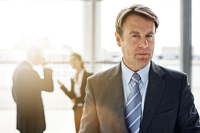 Buy stock photo Cropped portrait of a businessman standing a lobby with his colleagues in the background