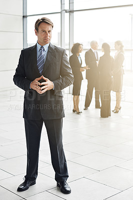 Buy stock photo Full length portrait of a businessman standing a lobby with his colleagues in the background