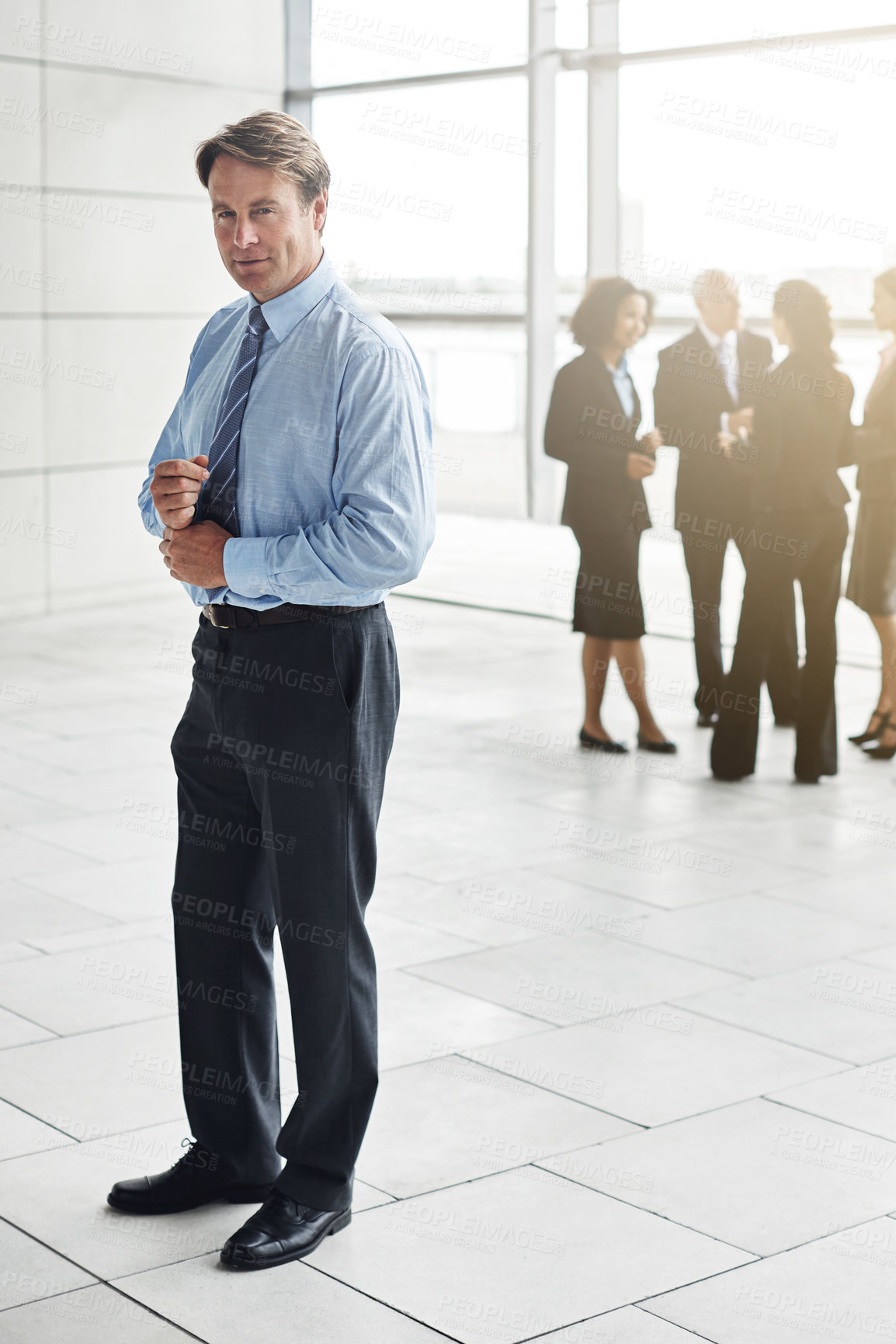 Buy stock photo Full length portrait of a businessman standing a lobby with his colleagues in the background