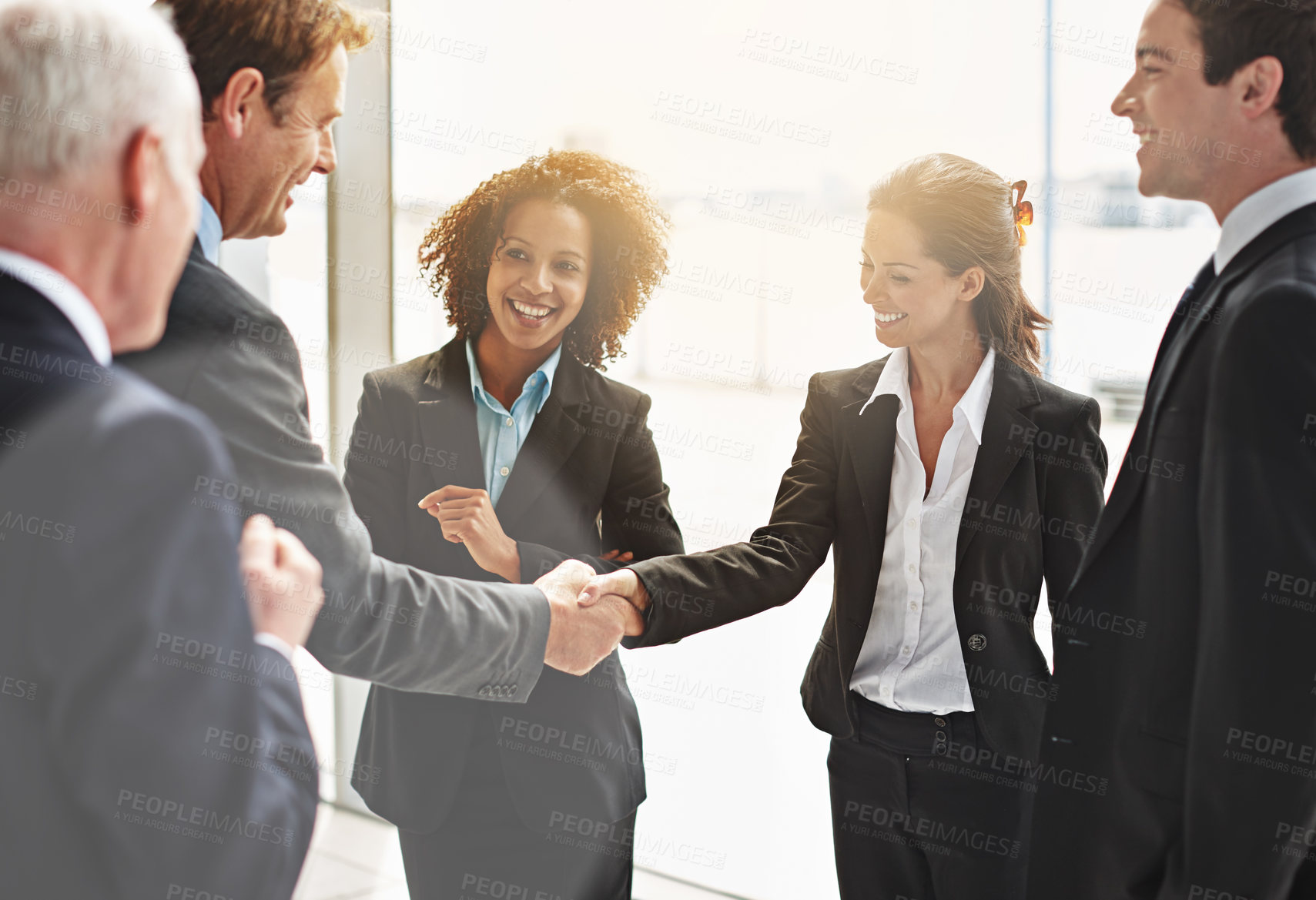Buy stock photo Cropped shot of two businesspeople shaking hands while their colleagues look on