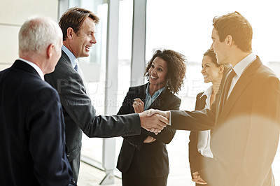 Buy stock photo Cropped shot of two businesspeople shaking hands while their colleagues look on