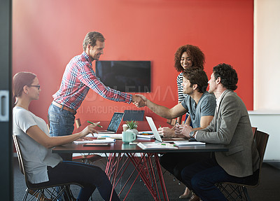 Buy stock photo Shot of a two people shaking hands in a boardroom while colleagues look on