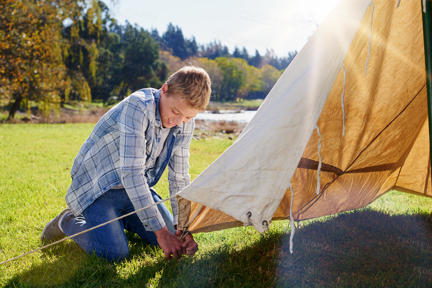 Buy stock photo Boy, camping and pitching tent in outdoor for vacation with family adventure, fresh air and lens flare. Smiling kid, shelter and green grass for safety with fun, summer holiday and sunshine in Canada