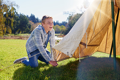 Buy stock photo Kid, camping and pitching tent in outdoor for vacation with adventure, fresh air and lens flare. Smiling boy, shelter and green grass for safety with fun, summer holiday and sunshine in Canada