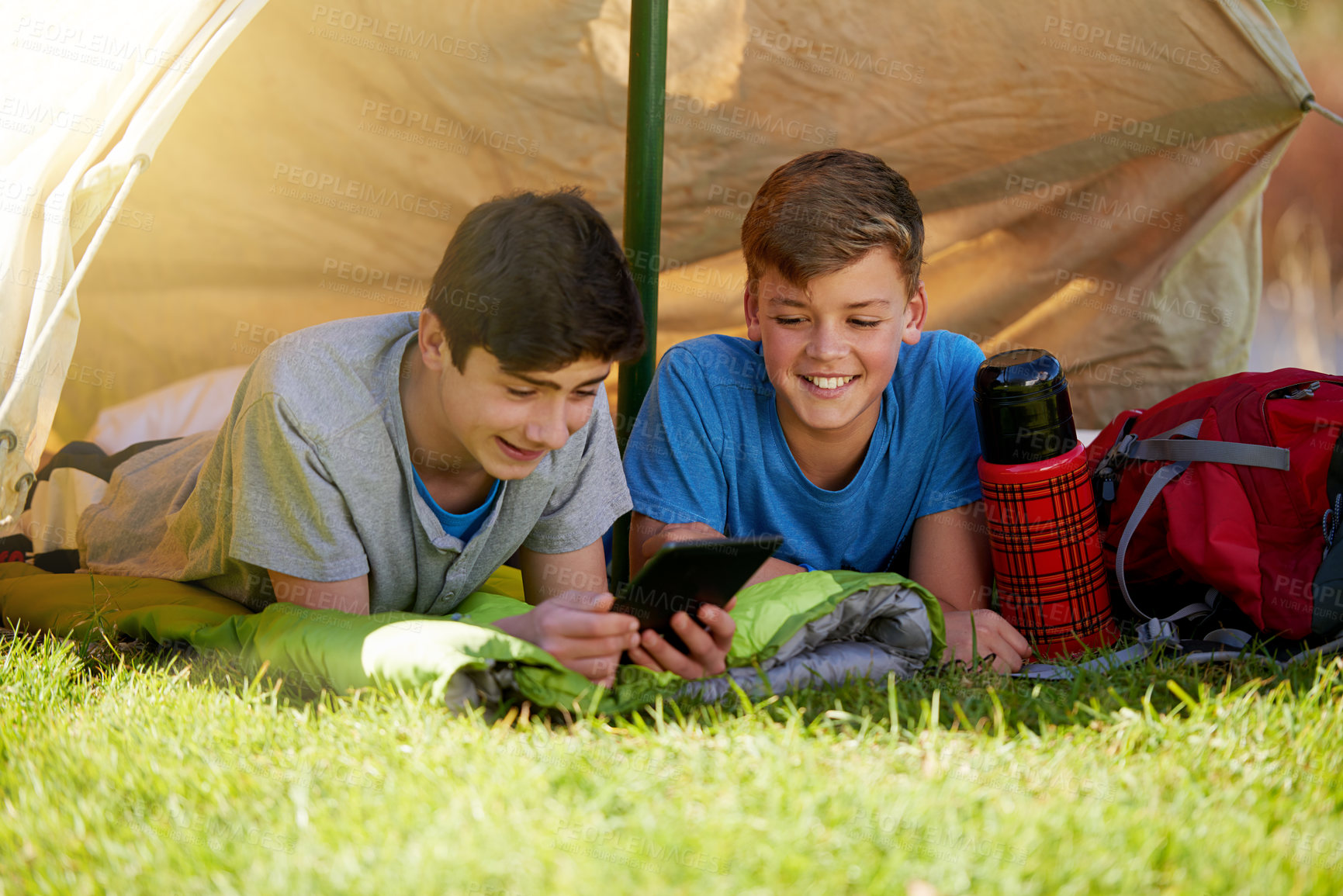 Buy stock photo A young boy showing his friend something on a digital tablet while they're camping