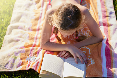 Buy stock photo Shot of a teenage girl lying on a towel while reading a book