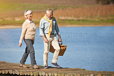 Buy stock photo Shot of a happy senior couple walking along the pier of a lake