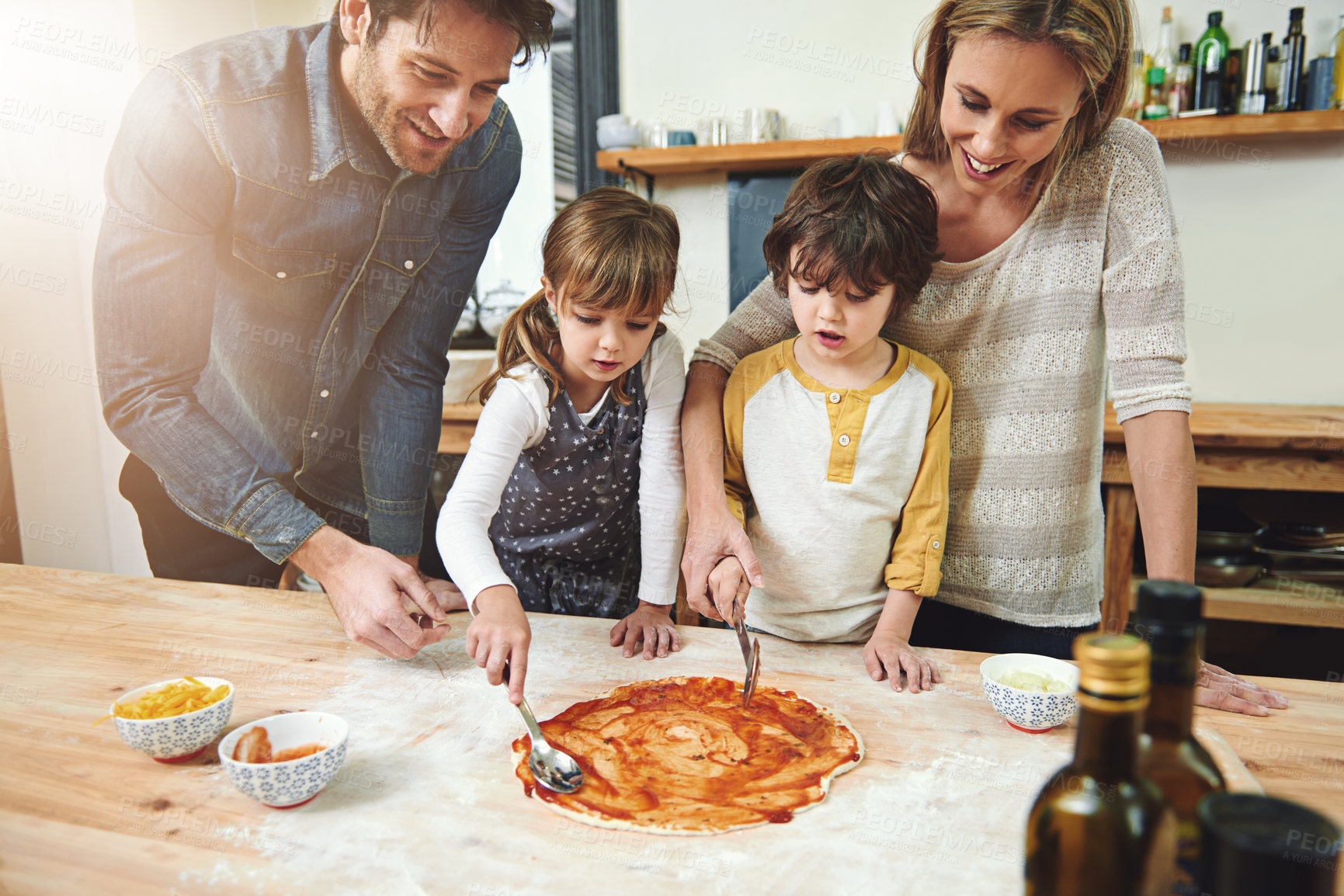 Buy stock photo Parents, kids and happy for cooking pizza with sauce, learning and helping hand for development in kitchen. Mother, father and children with dough, teaching and support with bonding in family house