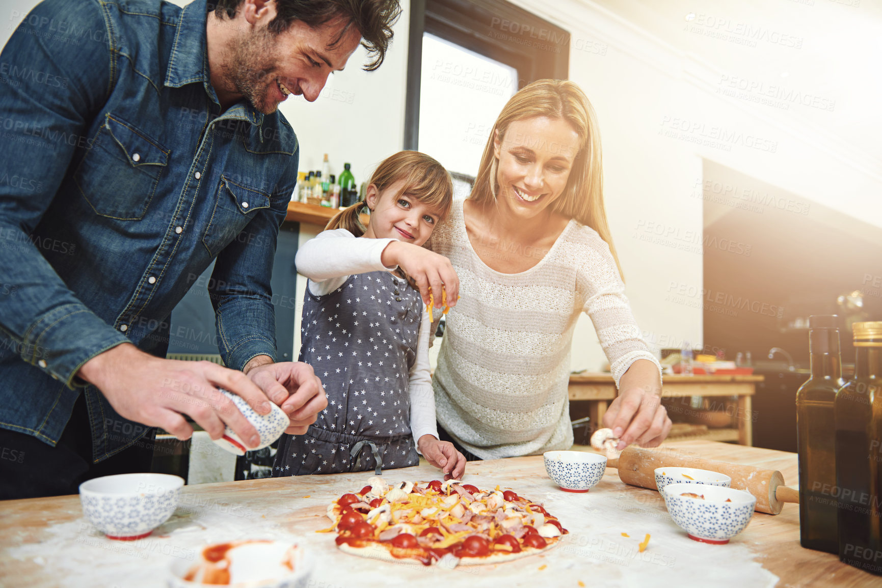 Buy stock photo Portrait, child and happy family baking pizza in kitchen together, bonding and smile for learning in home. Face, mother and father with girl cooking, teaching and help parents with cheese at table