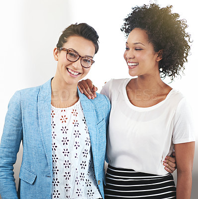 Buy stock photo Portrait of two female coworkers standing arm in arm in an office