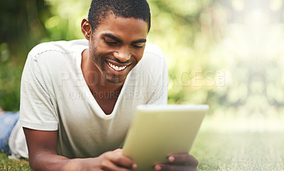 Buy stock photo Shot of a young man lying on the grass and using a digital tablet