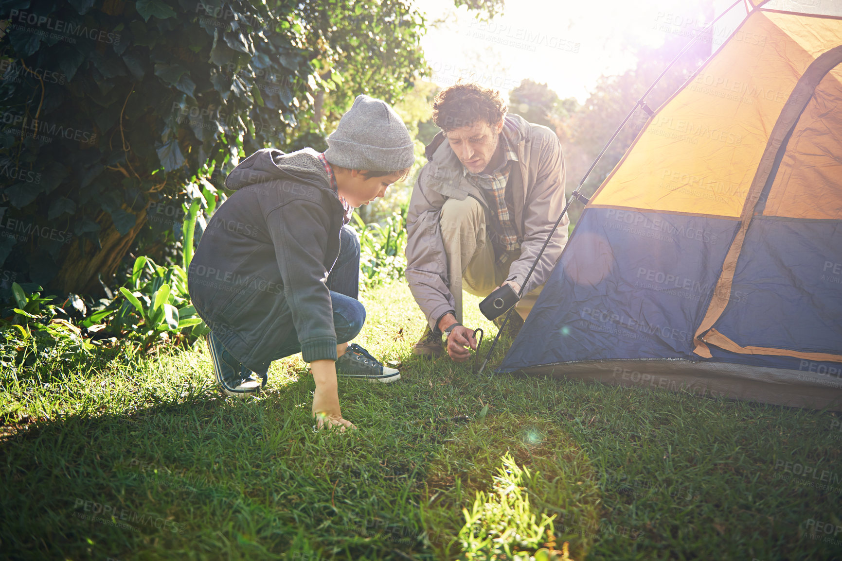 Buy stock photo Father, kid and hammer tent for camping outdoor in nature on vacation, bonding together and sunset. Dad, boy and preparing camp, learning and helping in forest for travel, education and adventure.