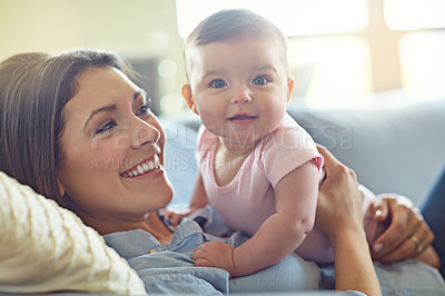 Buy stock photo Shot of a mother holding her baby girl while lying on a sofa