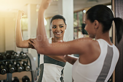 Buy stock photo A young woman flexing her muscles in front of the mirror at the gym