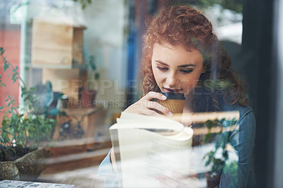 Buy stock photo A young woman drinking coffee while reading a book at a cafe