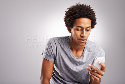 Buy stock photo Shot of a young man using his cellphone against a gray background