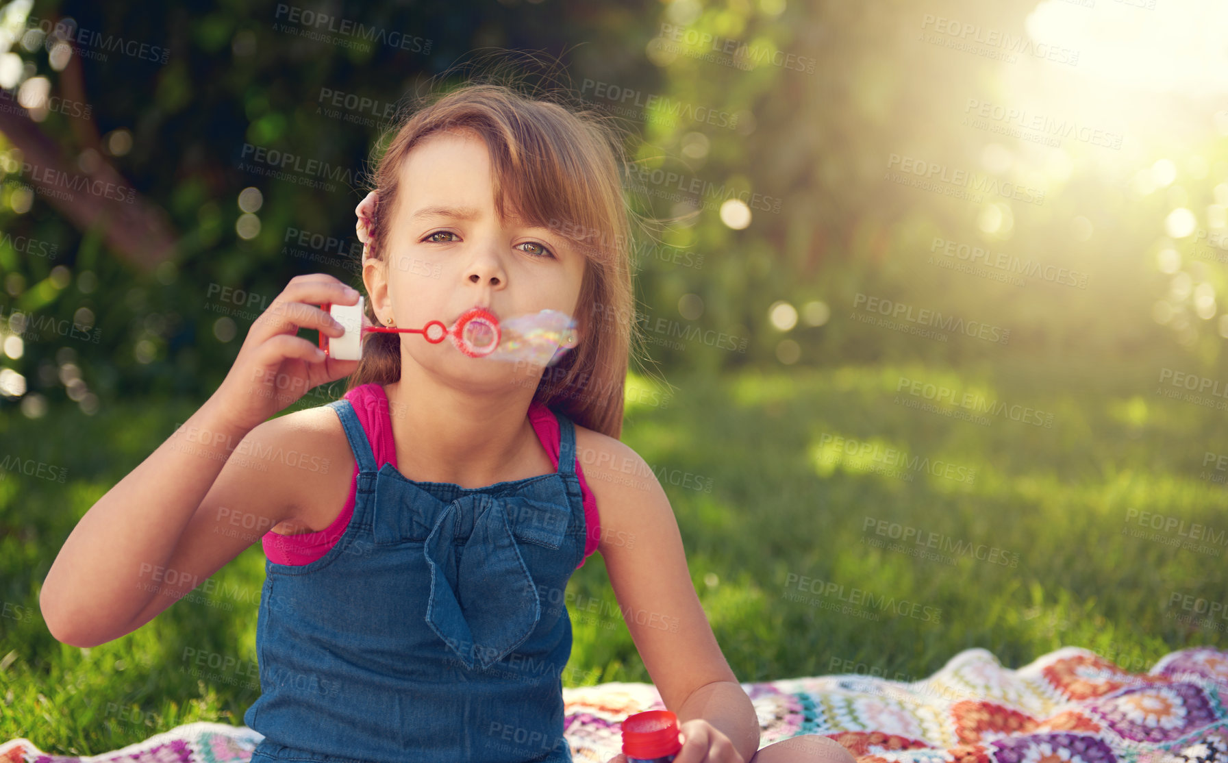 Buy stock photo Park, portrait and child blowing bubbles on grass in nature, relax and kid having fun on blanket outdoor. Toy, garden and face of girl with soap on summer vacation for recreation, game or leisure