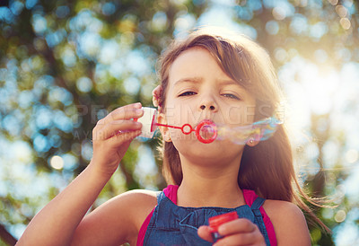 Buy stock photo Shot of a cute young girl blowing bubbles outside