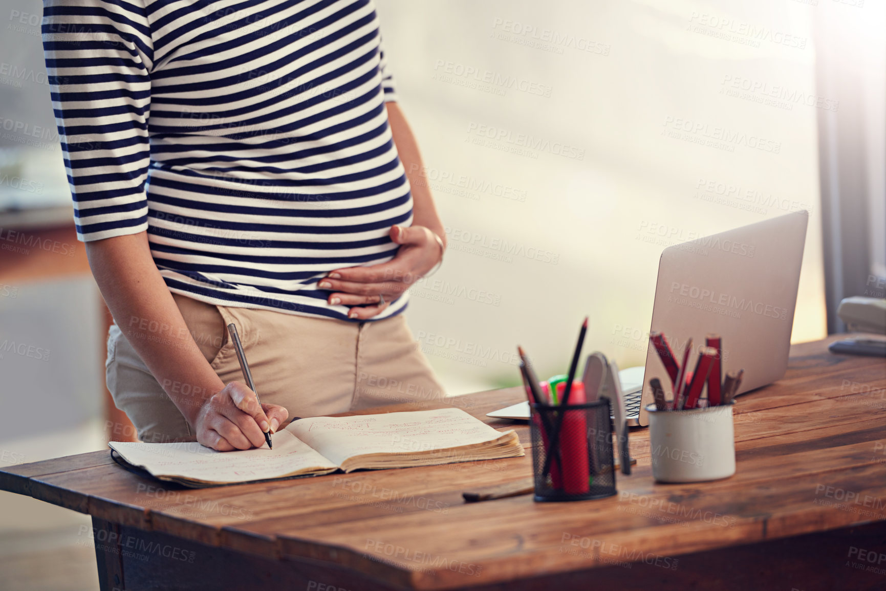 Buy stock photo Cropped shot of a young pregnant woman writing in her diary while standing in her office