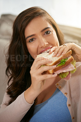 Buy stock photo Shot of a young woman taking a bite out of a sandwich