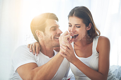 Buy stock photo Love, happy couple eat chocolate in bedroom and care with smiling or laughing. Valentines day, married people sharing sweet snack and spending quality time in their home and romance or caring