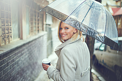 Buy stock photo Rearview portrait of an attractive young woman walking in the rain with an umbrella and a coffee