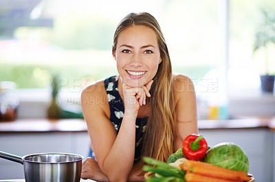 Buy stock photo Portrait of a young woman leaning on her kitchen counter with a pot and vegetables next to her