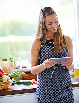 Buy stock photo A young woman using her digital tablet in her kitchen
