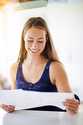 Buy stock photo Shot of a young woman reading paperwork at home