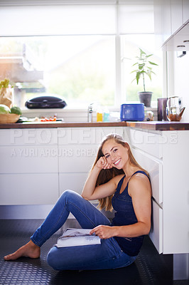 Buy stock photo Shot of a woman reading a magazine on her kitchen floor