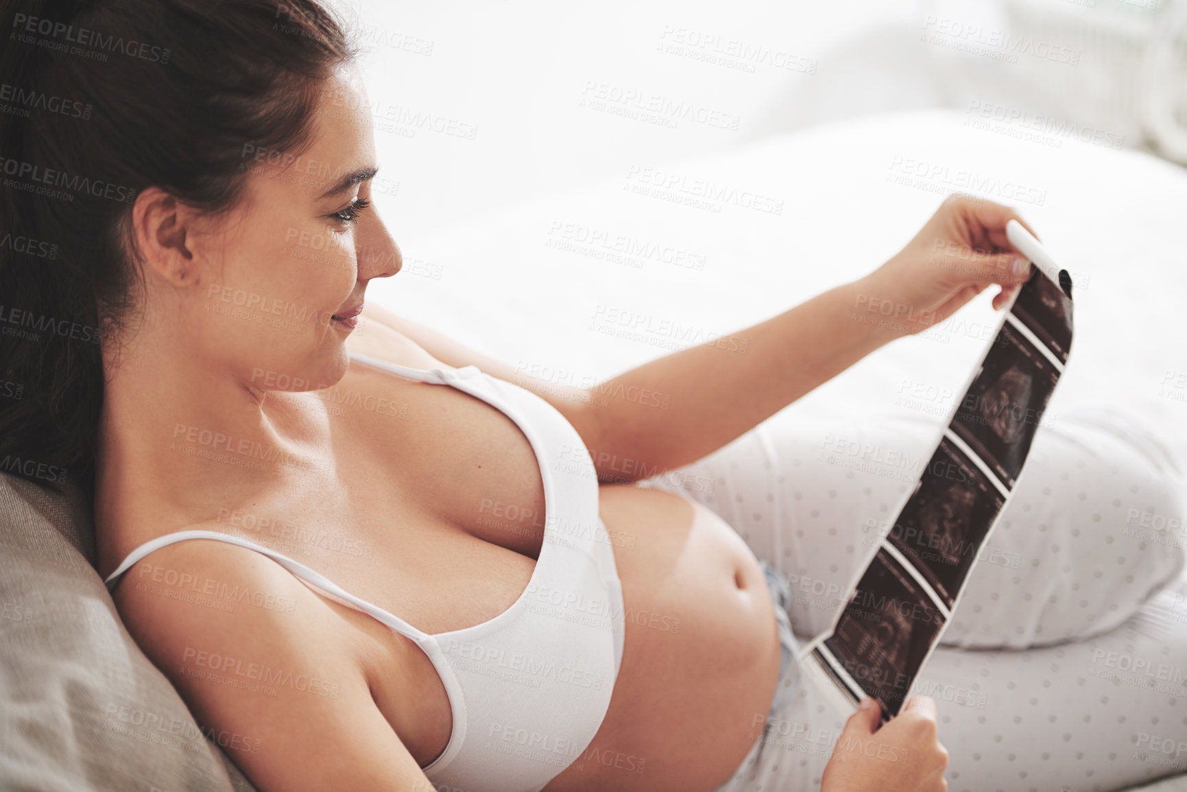 Buy stock photo Shot of a pregnant woman looking at a sonogram picture at home